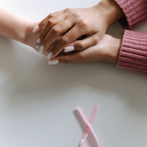 Close-up of two hands holding with a pink ribbon symbolizing cancer awareness.